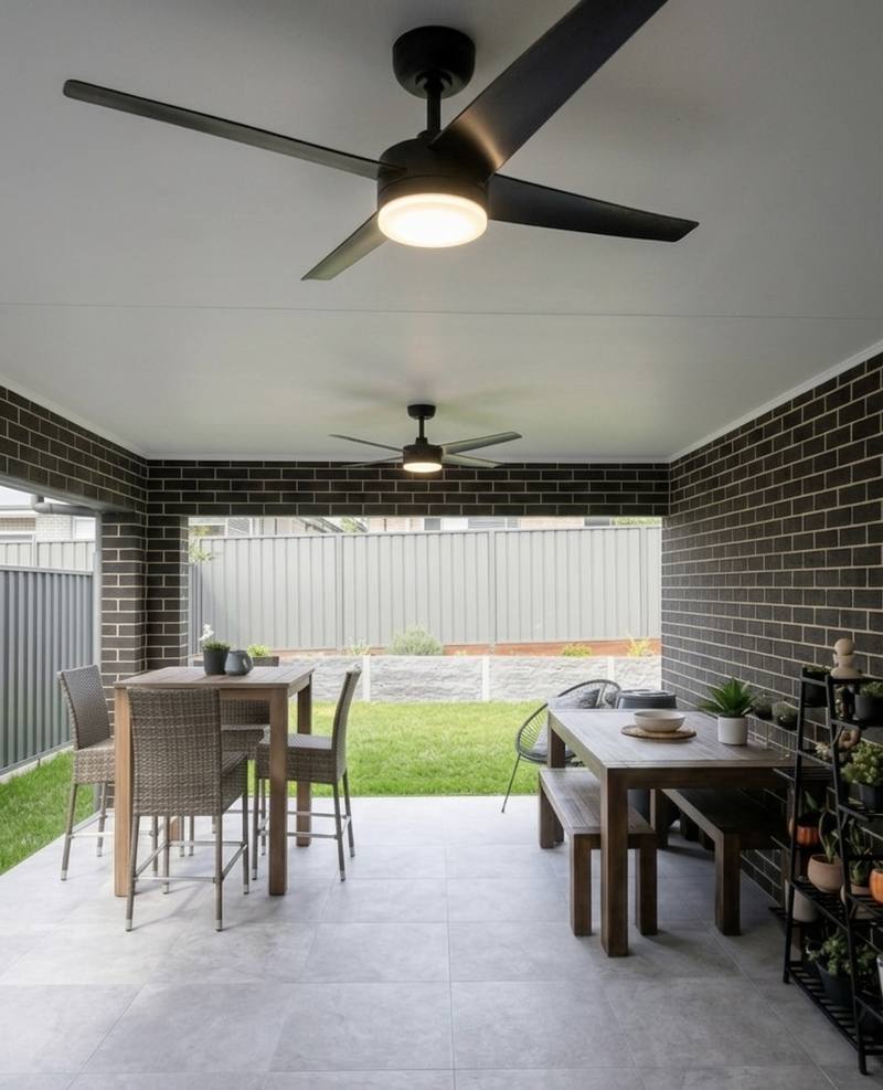 Two black ceiling fans with lights installed in an outdoor alfresco area